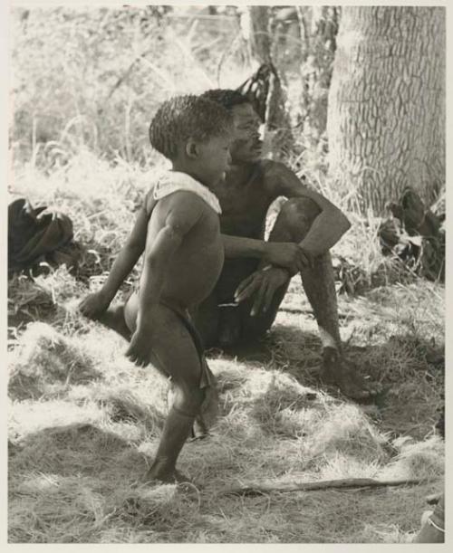 "Gao Medicine" sitting in his living place under a tree, with /Gaishay standing in front of him