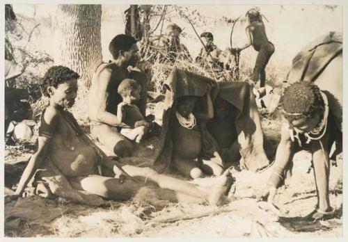 Group of children under a kaross, Debe sitting in his father's lap, and /Naoka and Di!ai sitting
