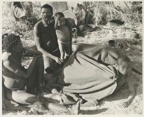 Debe sitting in his father's lap next to /Naoka and Di!ai, and a group of children under a kaross, including U's son /Gaishay
