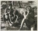 Di!ai and !U sitting, and Debe playing with a broken bowl