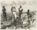 "Old Gau" standing with his bandaged foot in a bucket, with Elizabeth Marshall Thomas, Robert Story, Kernel Ledimo, and other unidentified people present
