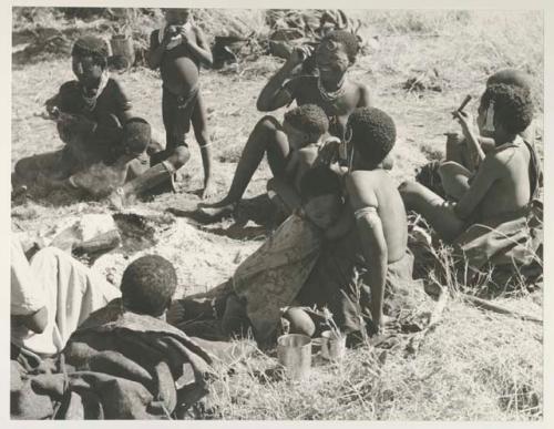 Group of seated women and children including !U, laughing, with !Ungka Norna, her two sons, Tsmagao and /Gaishay, //Kushay holding "Little ≠Gao" in her lap who is possibly nursing, and other unidentified people
