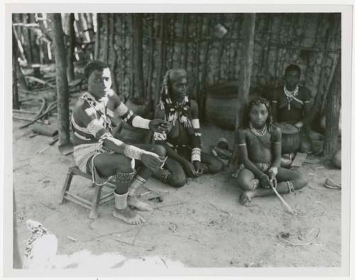 Makiena sitting on a stool in her kraal; visiting her are her son's wife, Rungiero, and her son's wife's sister (print is a cropped image)