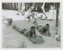 Two men lying on the ground inside Muremi's kraal with grain mortars in the background (print is a cropped image)