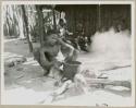 Boy putting a pot on the fire with Makiena and her daughter-in-law and other unidentified people in the background (print is a cropped image)