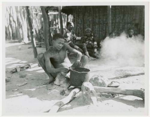 Boy putting a pot on the fire with Makiena and her daughter-in-law and other unidentified people in the background (print is a cropped image)