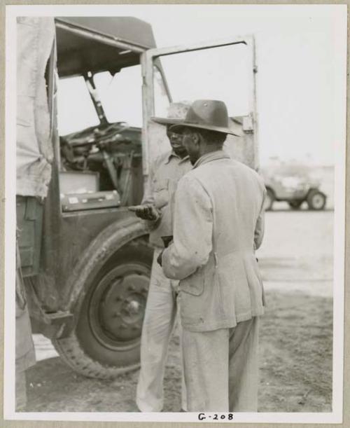 Muremi (right) and the driver standing by the door of one of the WNLA (Witwatersrand Native Labor Association) trucks, the driver giving something to Muremi (print is a cropped image)