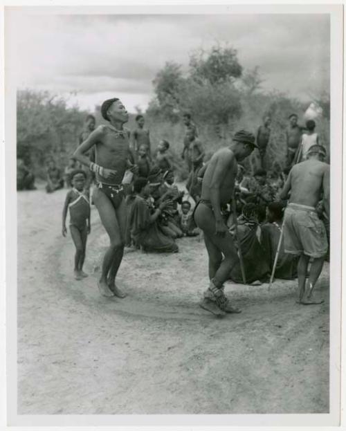 Men dancing in a circle behind the women (print is a cropped image)