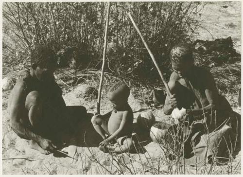 Oukwane and //Kuǂtera sitting beside their fire, N!whakwe sitting with them (print is a cropped image)