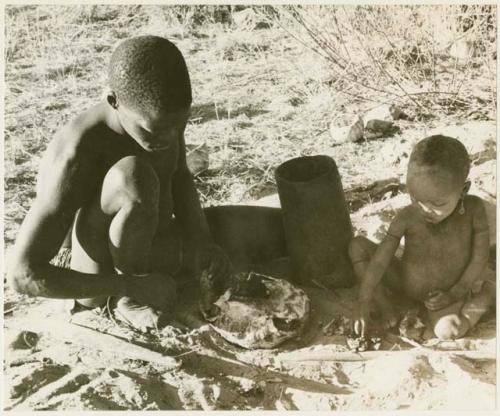 !Gai cutting into a turtle with a fire paddle, N!whakwe sitting beside him (print is a cropped image)