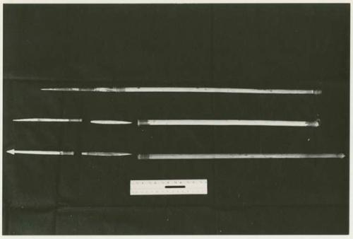 Three arrows against a black background with a ruler for measurement; shows bone point, connecting link, and shaft separated (print is a cropped image)