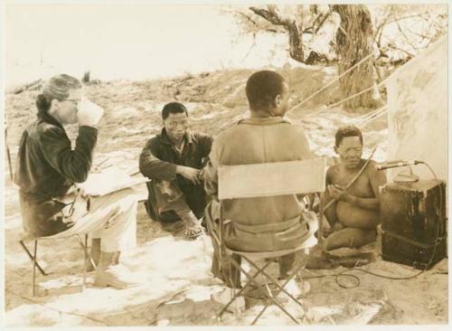 Oukwane playing the musical bow while Lorna Marshall, Kernel Ledimo, and Dabe record; Lorna Marshall drinking tea (print is a cropped image)