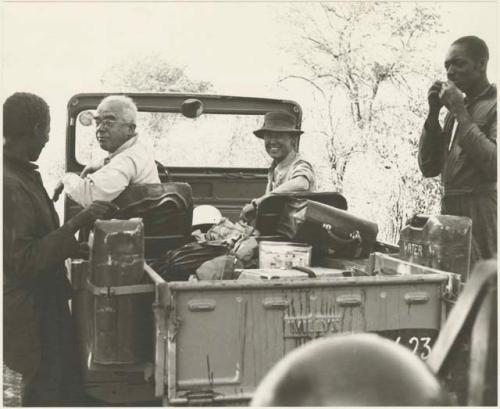 Laurence Marshall and Lorna Marshall sitting in the expedition Jeep, with two men present

