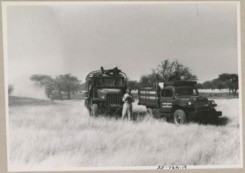 Two expedition trucks, with Daniel Blitz holding a camera in front of them

