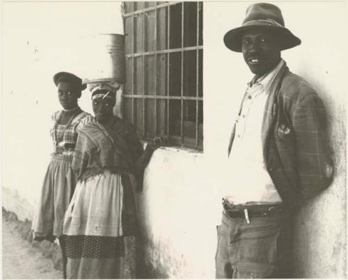 Man and two girls standing leaning against the wall of a store at Sehitwe
