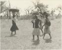 Three women walking with goods piled on their heads with a girl





