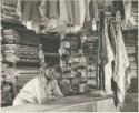 Interior of a trader's store at Sehitwe, with a man standing behind a counter












