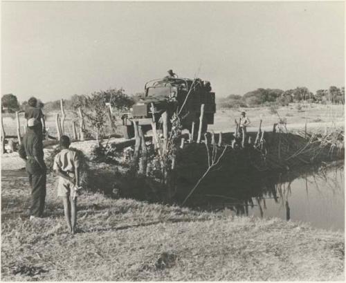 GMC truck crossing a bridge, with expedition members watching, seen from a distance










