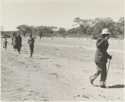 Man in a pith helmet walking, followed by a group of people








