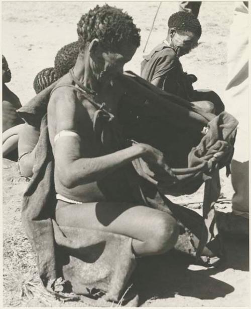 Woman holding out her kaross for tobacco, with other people in the background






