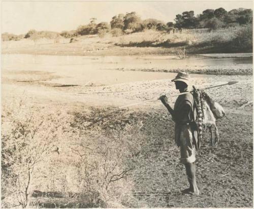 Man standing with skins hanging from his spear next to the Taoge River

