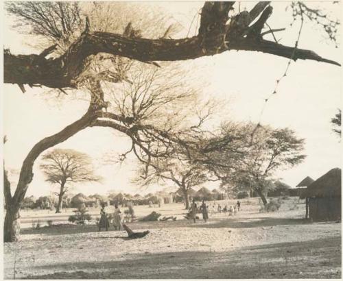 Women walking, and a group sitting, with huts in the distance

