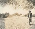 Man standing, with view of huts and buildings of Tsau in background
