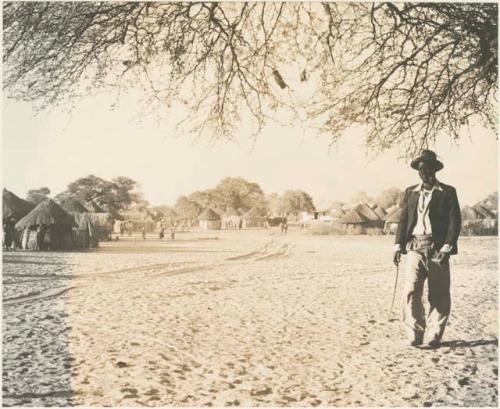 Man standing, with view of huts and buildings of Tsau in background
