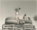 Simon Molamo, Casper Kruger and another person sitting and standing on top of GMC tires on the top of an expedition truck


