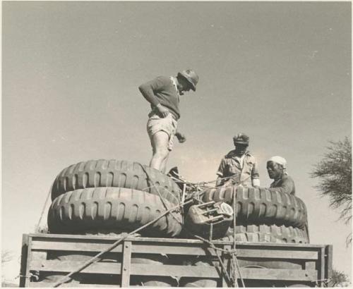 Simon Molamo, Casper Kruger and another person sitting and standing on top of GMC tires on the top of an expedition truck


