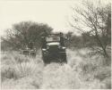 Man sitting on top of an expedition truck (Dodge) atilt in the track, and another man sitting in a Jeep next to it


