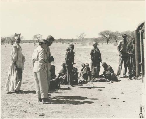 Group of people sitting and standing, including a Herero woman, Laurence Marshall and Daniel Blitz
