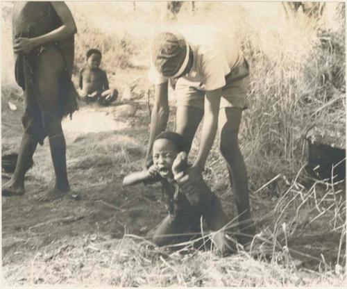 /Gishay ("Old Gau's" son) holding "Little ≠Gao" who is crouched on the ground, struggling







