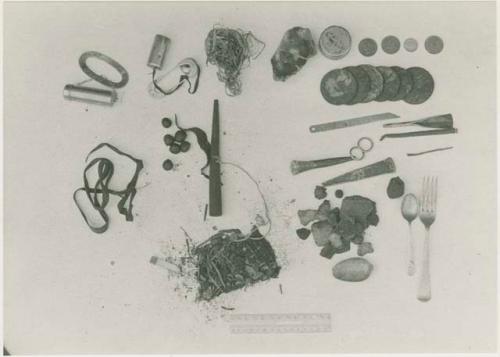 Contents of bag including oracle disks, fire-strikers, tinder, a pipe, sinew, a European fork and spoon, scrapers, drills, a cigarette butt, possibly tobacco, and possibly tsi, next to a ruler for measurement





































