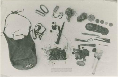 Bag and its contents including oracle disks, fire-strikers, tinder, a pipe, sinew, a European fork and spoon, scrapers, drills, a cigarette butt, possibly tobacco, and possibly tsi, next to a ruler for measurement







































