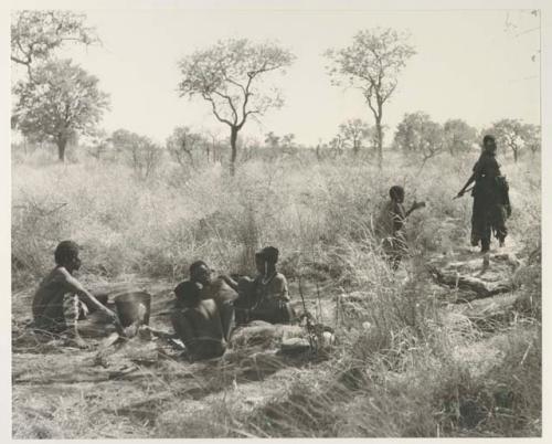 "Old Gau" with a group of unidentified people, all seated, and a bucket

