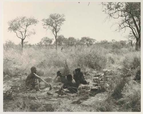 "Old Gau" with a group of unidentified people, all seated, and a bucket