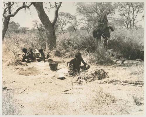 "Old Gau" seated and three unidentified children and other people in the background, middle distance scene
