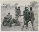 Medicine man held by /Gunda and another person, with "/Qui Navel" holding one of his children and other people present
