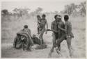 Medicine man held by /Gunda and another person, with "/Qui Navel" holding one of his children and other people present
