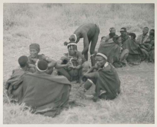 Medicine man curing someone in a seated group
