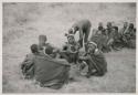 Medicine man curing someone in a seated group
