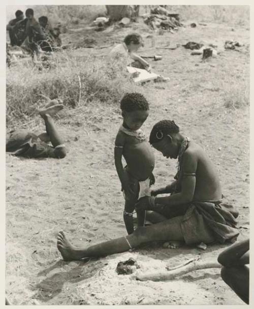 !U adjusting beads on !Ungka Norna's leg and Elizabeth Marshall Thomas taking notes; other unidentified people in the background


























