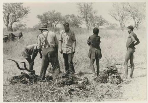 ≠Toma wearing a coat, standing with "Crooked /Qui," Wilhelm Camm and John Marshall next to kudu meat



























