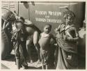 N!ai, /Gaishay (Di!ai's son), a girl, and a boy standing in front of an expedition truck  with "Peabody Museum of Harvard University" showing 

























