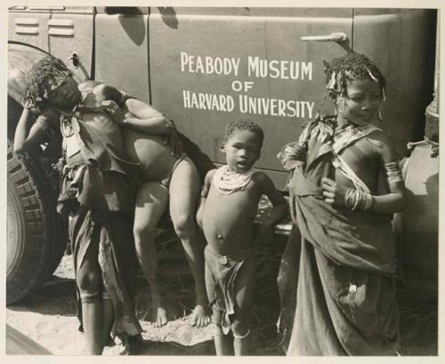 N!ai, /Gaishay (Di!ai's son), a girl, and a boy standing in front of an expedition truck  with "Peabody Museum of Harvard University" showing 

























