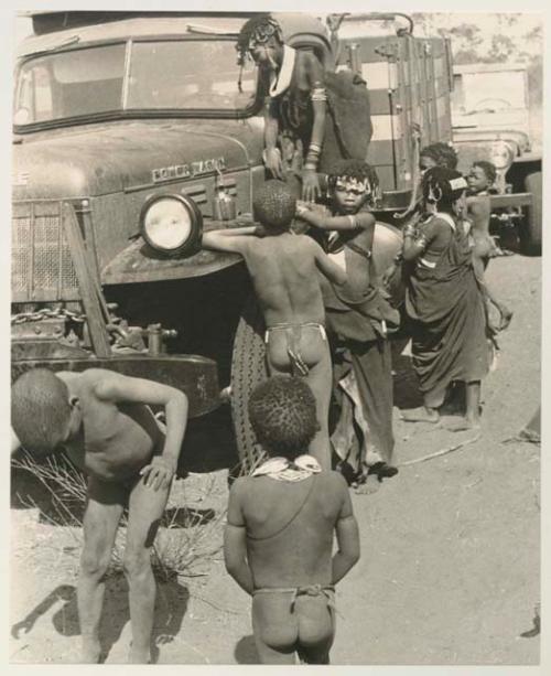 Children beside an expedition truck, including N!ai wearing a kaross























