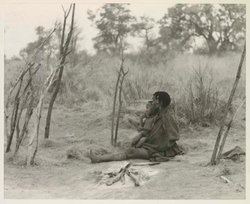 Woman seated by her fire, holding a child






















