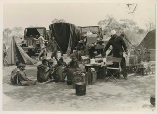 Expedition camp with Ju/'hoansi sitting in the midst; Philip Hameva holding teacups























