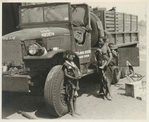 N!ai leaning against one of the expedition's GMC trucks, along with Di!ai (wife of ≠Gao) carrying a baby on her back























